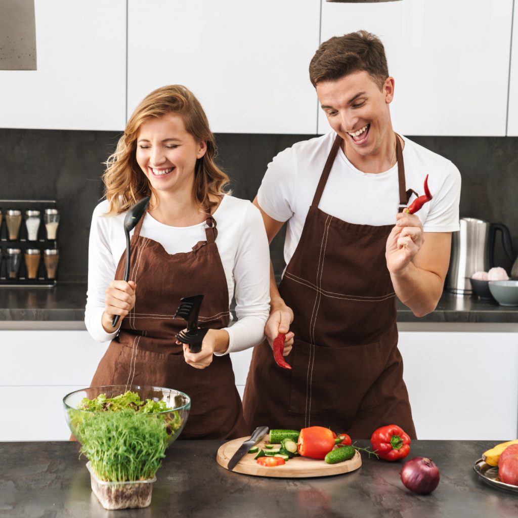 A man and women prepare food for their meal prep business in a kitchen wearing brown aprons. 